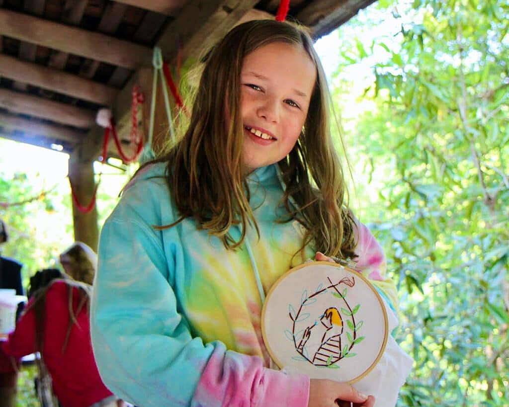 camp girl holding needlepoint project