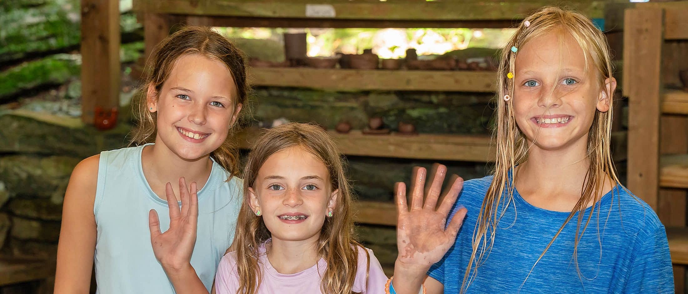 Three children smiling and showing their clay-covered hands during a pottery class indoors.