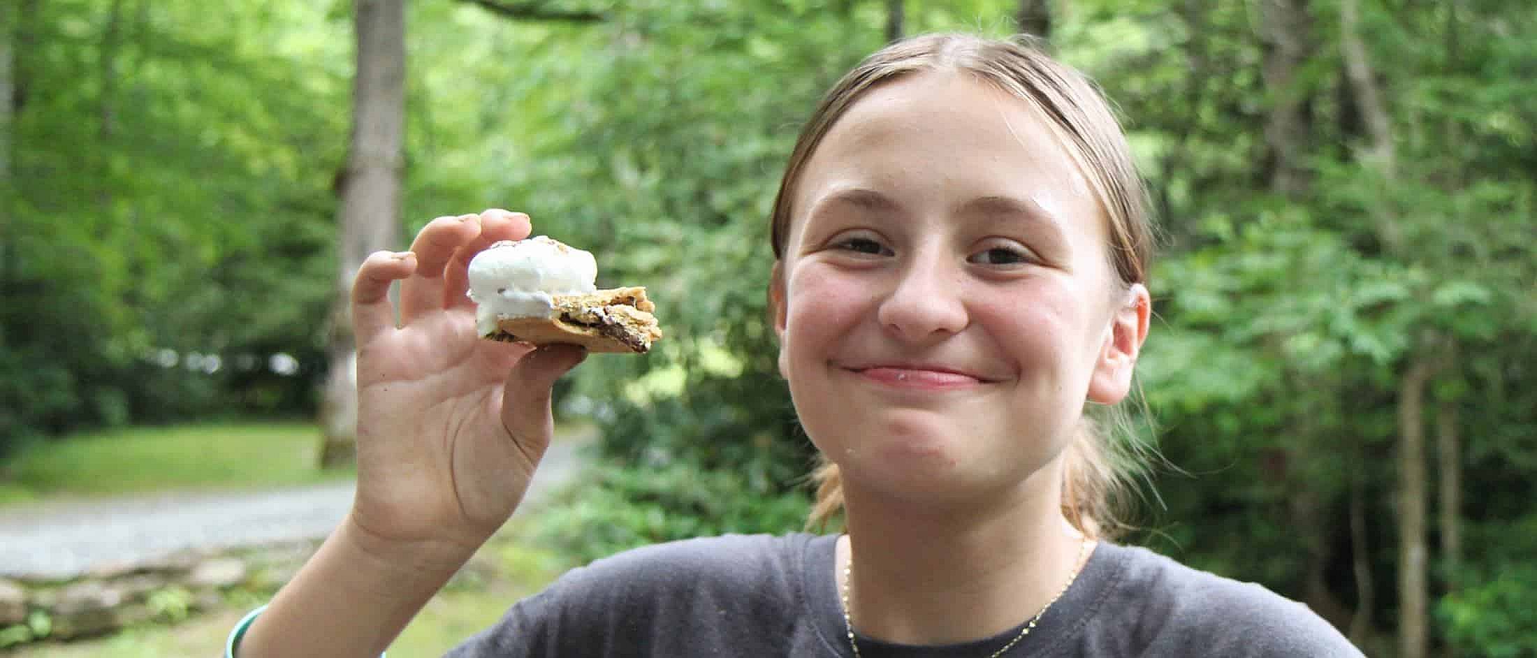 camp teenage girl holding a freshly made s'more saying yum