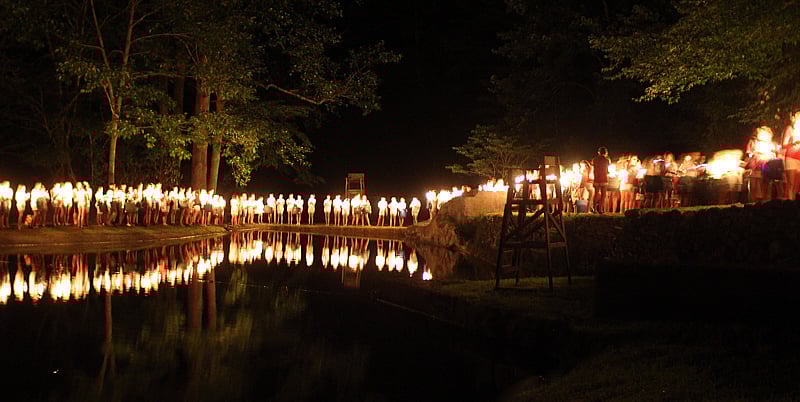 Campers with lit candles around lake
