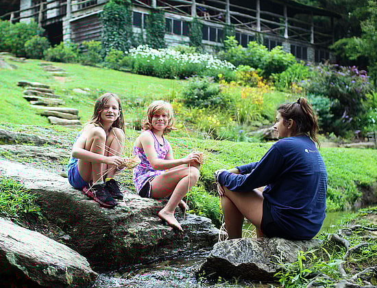 Two girls and counselor weaving baskets by the creek