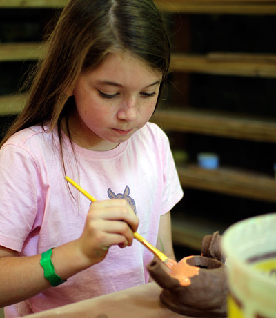 Child glazing a pottery teapot