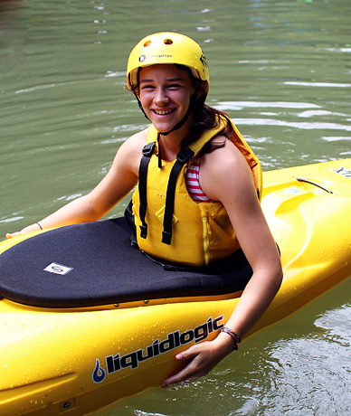 Camp girl smiling in yellow kayak with yellow helmet and pfd