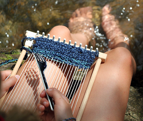 Camp girl using lap loom with feet in creek