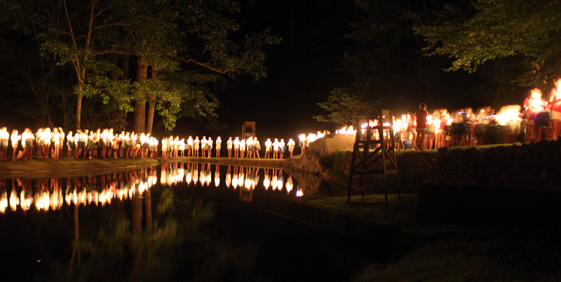 Campers with lit candles around lake