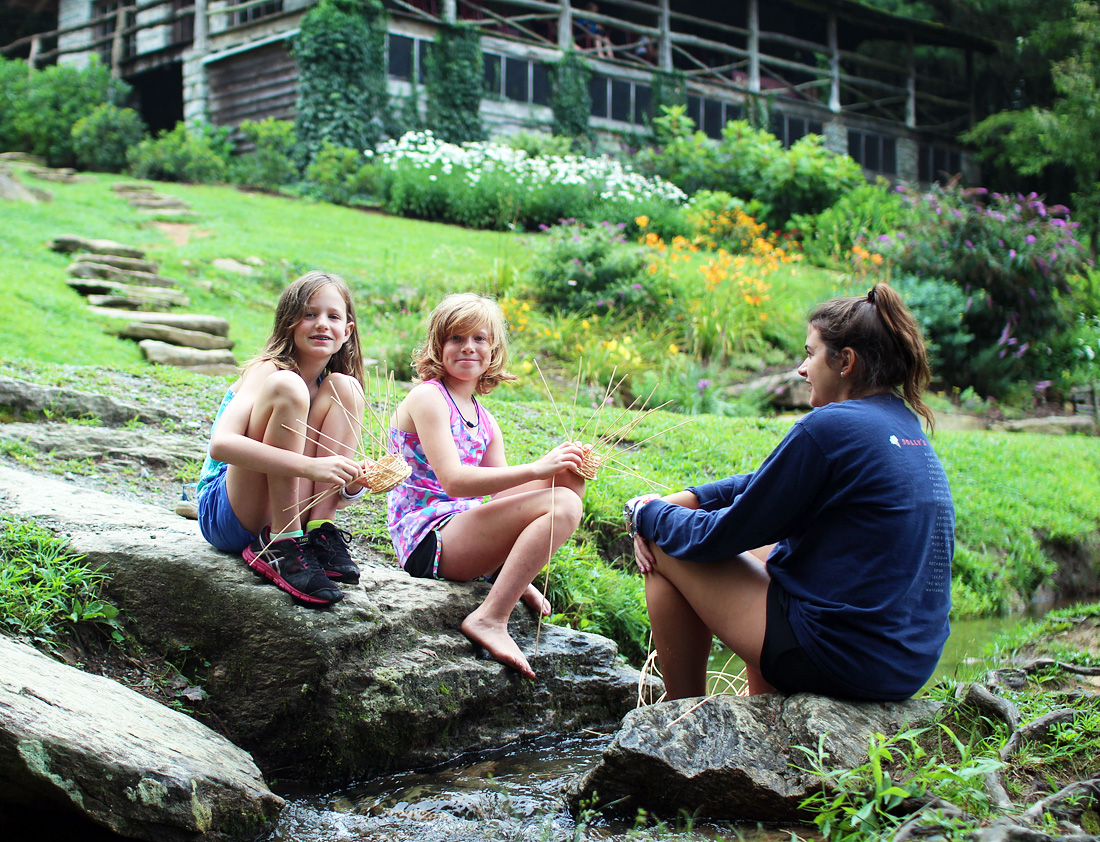 Two girls and counselor weaving baskets by the creek