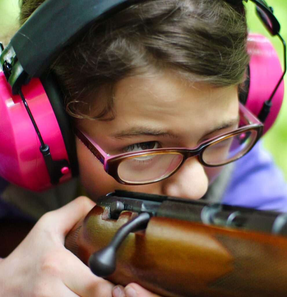 camp girl carefully aiming rifle