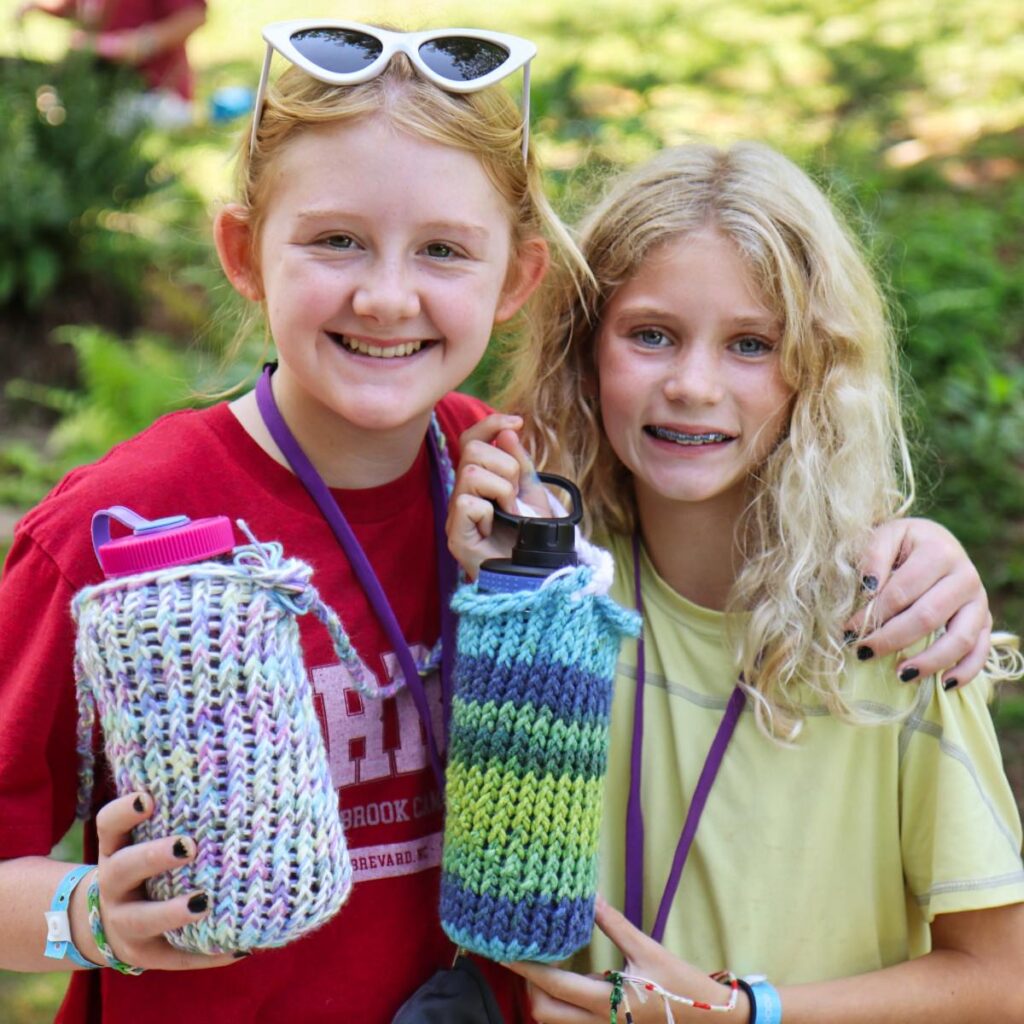 camp girls showing their knitted water bottle covers